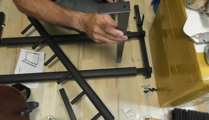 Insert the angled brackets (one per leg) into the upright supports and attach using the provided bolts and wing nuts. Note that the brackets are designed to be angled for guitar support, preventing toppling.