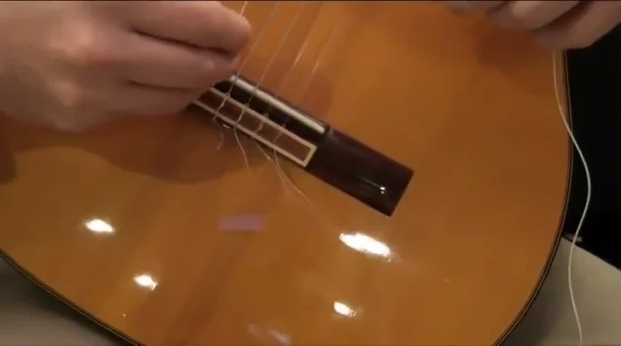 Tie a simple knot at the end of the string on the bridge (loop it across once, then under itself twice).