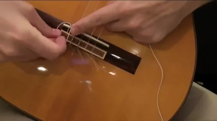 Tie a simple knot at the end of the string on the bridge (loop it across once, then under itself twice).