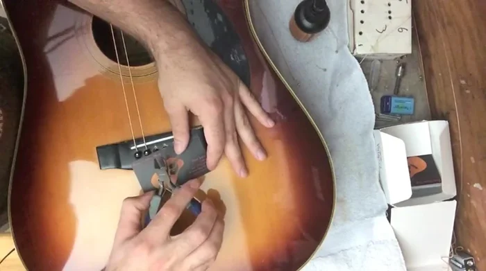 Carefully use string cutters to grip the bottom of the bridge pin and leverage it out. Be cautious not to cut the bridge pin itself.